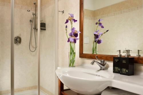 a bathroom with a sink and a vase of purple flowers at Relais Villa Monte Solare Wellness & SPA in Panicale