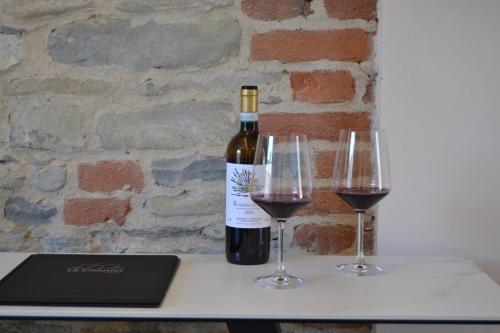 una botella de vino y dos copas de vino en una mesa en Le Cornici - Cascina di Charme en Diano dʼAlba