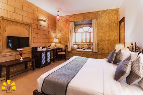 a bedroom with a bed and a desk and a television at Hotel Golden Haveli in Jaisalmer