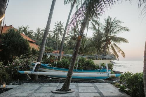a blue boat parked next to a beach with palm trees at ALOKA BAHARI Villas in Tejakula