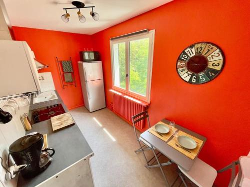 a kitchen with an orange wall with a clock on the wall at Studio au pied du Vercors in Saint-Jean-en-Royans