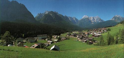 a village on a hill with mountains in the background at Appartamenti Kratter Pietro in Sappada