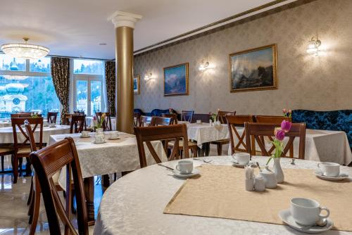 un comedor con mesas y sillas blancas y ventanas en Spa Hotel Schlosspark, en Karlovy Vary