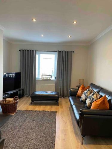 a living room with a black leather couch and a window at Lovely 2 bed apartment with hot tub log burner and off street parking in Dumfries