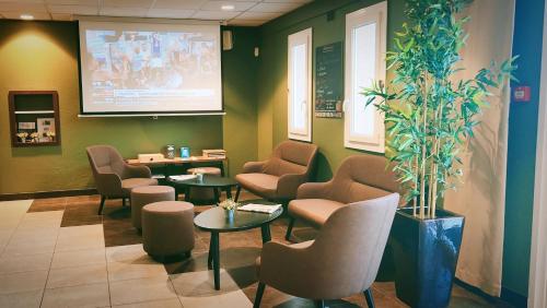 a waiting room with chairs and tables and a large screen at Kyriad Libourne Saint Emilion in Arveyres