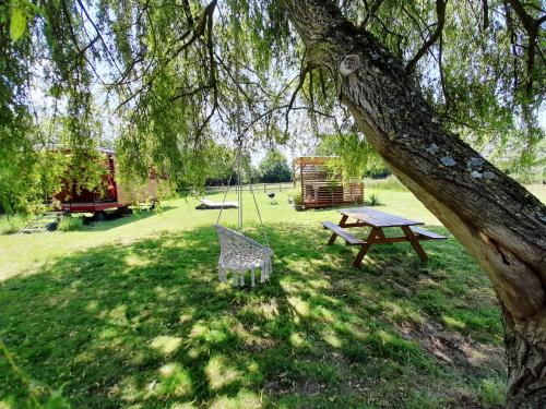 une table de pique-nique et un banc sous un arbre dans l'établissement Jolie roulotte au bord de la mare, à La Bretauche