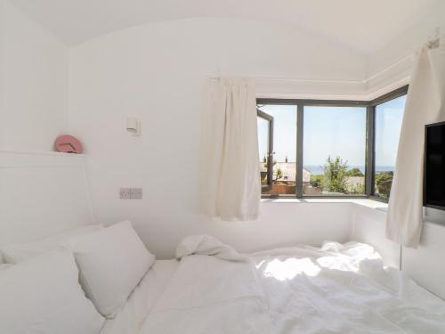 a white bedroom with a bed and a window at Little Pip in Penzance