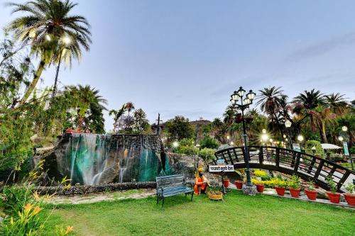 a waterfall in a park with a bench and a bridge at Chacha Inn The Garden Retreat in Mount Ābu