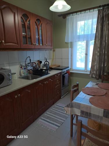 una cocina con armarios de madera, mesa y fregadero en Széll 3 Apartman, en Szombathely
