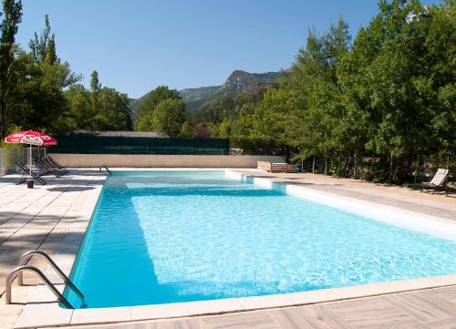 une grande piscine bleue avec un parasol dans l'établissement Camping L'Ondine de Provence, à La Motte-Chalançon