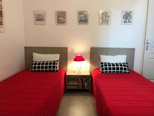 2 lits dans une chambre avec des draps rouges et une lampe dans l'établissement VILLA DU GOLFE T3 Beaurivage, à La Ciotat