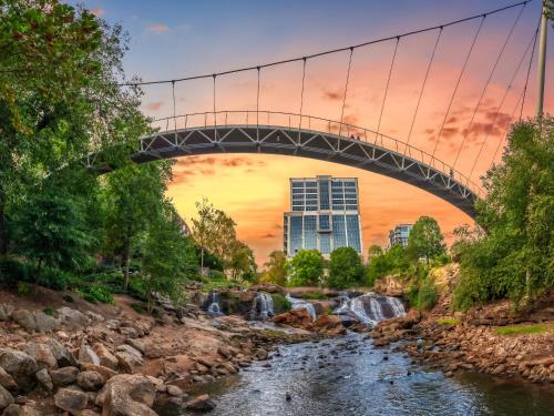 eine Brücke über einen Fluss mit einem Wasserfall in der Unterkunft Midtown Suites - Greenville in Greenville