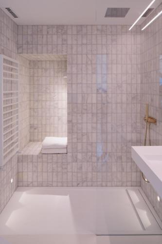 a white tiled bathroom with a shower with a bench at Eastside - Architect designed retreat with wood-fired sauna in Penicuik