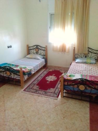 a bedroom with two beds and a red rug at Apartments in Attaouia Wonderful in Attaouiya ech Chaïbiya