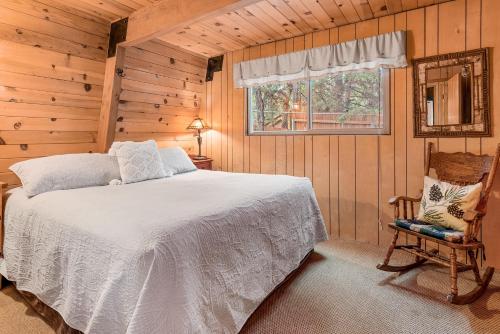 1 dormitorio con cama, ventana y silla en Zen Den - Beautiful A-frame cabin with classic brick wood burning fireplace and a hot tub, en Big Bear Lake