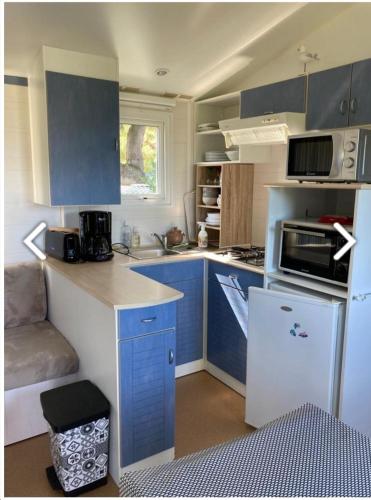 Elle comprend une petite cuisine avec des placards bleus et un réfrigérateur blanc. dans l'établissement Mobile-home 4 pers vue mer, à Saint-Cast-le-Guildo