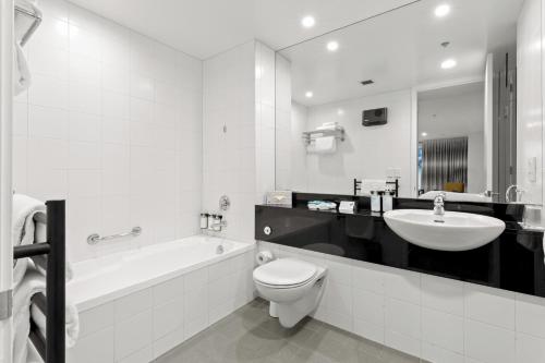 Scenic Suites Queenstown في كوينزتاون: حمام أبيض مع حوض ومرحاض وحوض استحمام