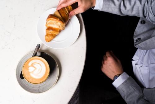 a person holding a plate with a cup of coffee and a pastry at voco Vienna Prater, an IHG Hotel in Vienna