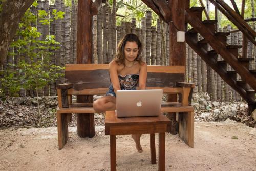 a woman sitting on a bench with a laptop at Casa Tulix Cabaña Tulum in Francisco Uh May