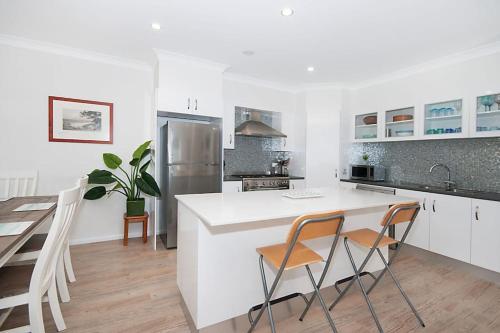 a white kitchen with a counter and chairs in it at LUXURY TOWNHOUSE! Walking distance to everything! in Yamba