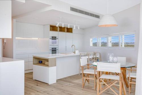 a kitchen with white cabinets and a table and chairs at Beachfront Bliss, 3BR Kirra Oasis- Pool and Sauna in Gold Coast