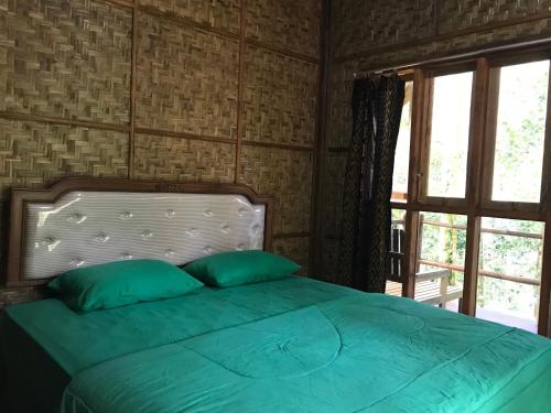 uma cama com almofadas verdes num quarto com uma janela em Joben Ecolodge em Tetebatu