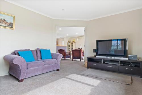 a living room with a purple couch and a tv at Bowentown Bach - Waihi Beach Holiday Home in Waihi Beach
