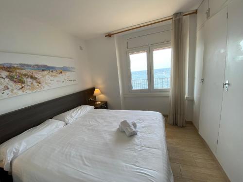 Cama blanca en habitación con ventana en Playa Canadell MAR G primera linea de mar con terraza, en Calella de Palafrugell