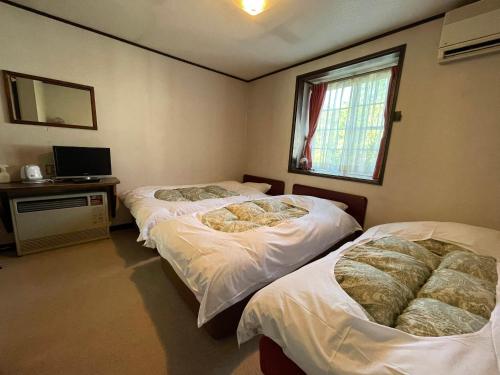 a bedroom with two beds and a desk and a window at Hotel Sejour Mint in Hakuba in Hakuba