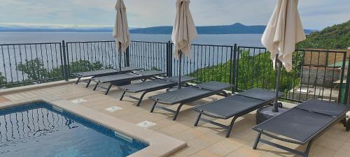 a pool with chairs and umbrellas on a balcony at Apartments Villa Elma in Mošćenička Draga