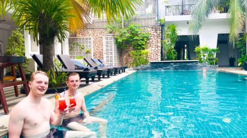 two men sitting in a swimming pool with drinks at Boutique Indochine d'Angkor in Siem Reap