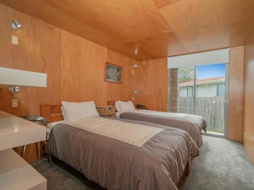 two beds in a room with wooden walls at Little Paua - Pauanui Holiday Home in Pauanui