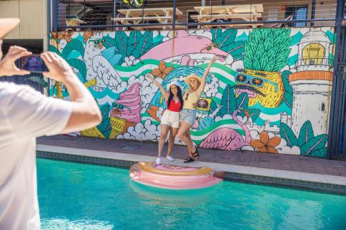 YHA Byron Bay في خليج بايرون: a woman taking a picture of two women standing on an inflatable circle in