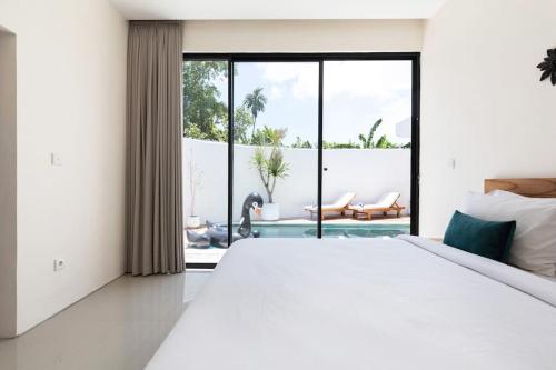 a white bedroom with a large bed and a large window at The R Villa Kaba - incl. Motorbikes in Seminyak