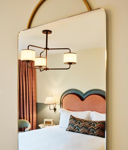 a mirror in a hotel room with a bed and a chandelier at The Hoxton, Charlottenburg in Berlin