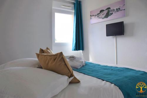 a bedroom with a bed with pillows and a tv on the wall at Adonis Grandcamp - Résidence Les Isles De Sola in Grandcamp-Maisy