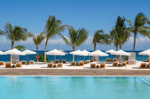 a swimming pool with chairs and umbrellas and the ocean at Aldiana Club Zanzibar Kwanza in Kizimkazi