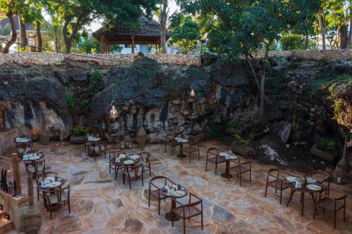 a restaurant with tables and chairs in front of a stone wall at Aldiana Club Zanzibar Kwanza in Kizimkazi