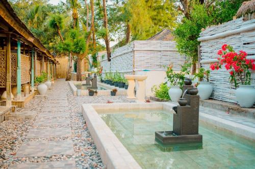 a garden with a fountain and some plants and flowers at Bungalow Cafe Gili Beachfront in Gili Meno