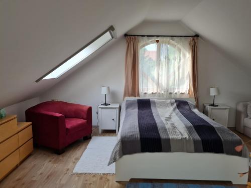 a bedroom with a bed and a red chair at Duzzogó Vendégház Agárd in Gárdony