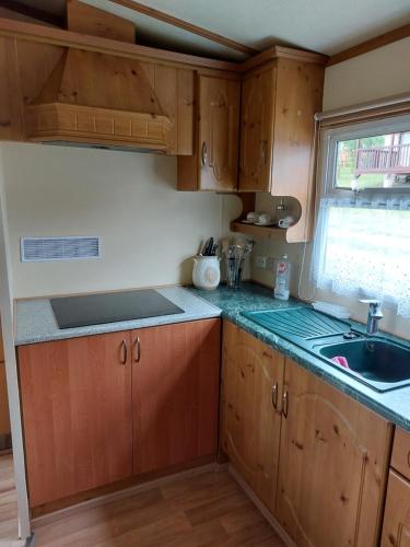 Una cocina con armarios de madera y un fregadero y una ventana. en Mobilní dům Rimini a Monaco v kempu ve Výrovicích, en Výrovice