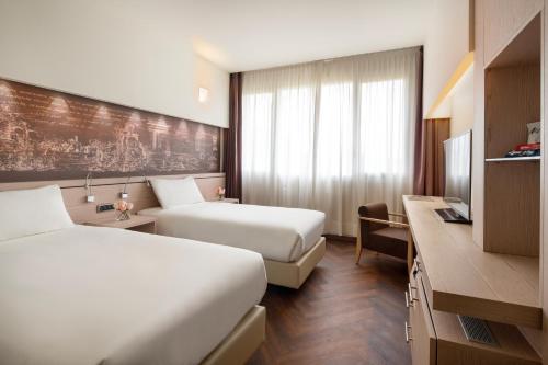 a hotel room with two beds and a desk at UNA Hotels Bologna San Lazzaro in San Lazzaro di Savena