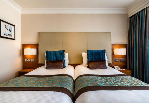 a hotel room with two beds with blue pillows at The Marble Arch Hotel, by Thistle in London