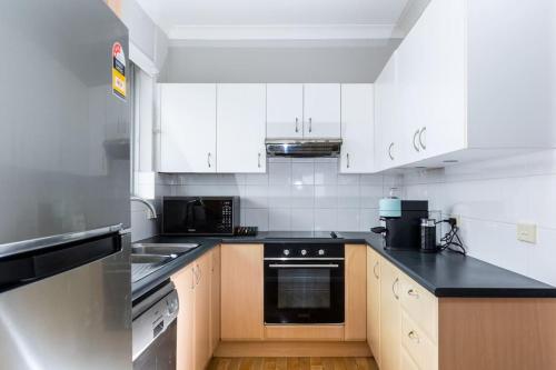 uma cozinha com armários brancos e um balcão preto em Mosman Views, 2bed, Parking, 15min Walk to Beach em Sydney