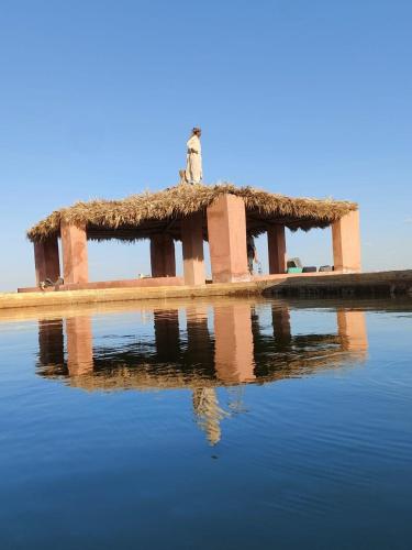 Mbiama Resort في سيوة: مبنى بسقف عشبي فوق سطح ماء
