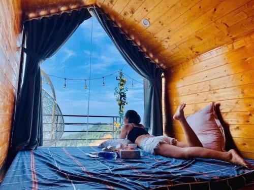 a woman laying on a bed in a room with a window at Tam Đảo Xanh Homestay - Venuestay in Vĩnh Phúc