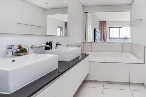 a white bathroom with two sinks and a mirror at Urban Oasis Apartments at One Hyde Park in Johannesburg