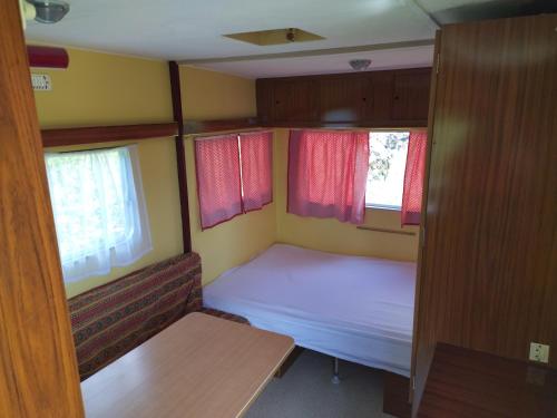 a small room with a bed and two windows at Camping La Fôret du Morvan Vintage caravan in Larochemillay