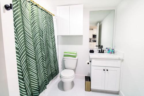 baño con aseo y cortina de ducha verde y blanca en Summer Tropics Studio Apartment Two Queen Beds, en Galveston