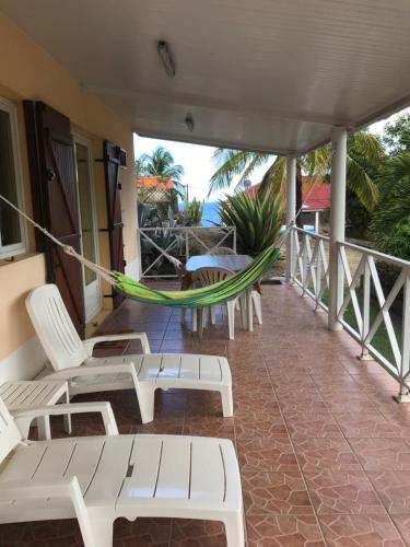 a porch with white chairs and a hammock at Studio proche mer & climatisé les Anses d'Arlet in Les Anses-dʼArlets